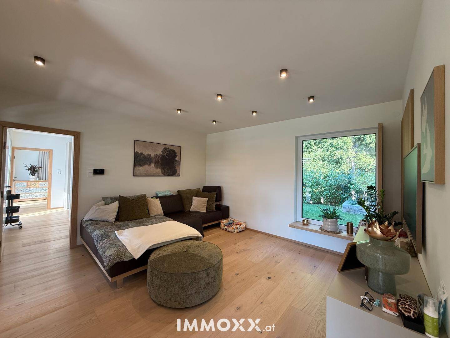 Gemütliches Wohnzimmer mit großem Sofa, Holzboden und weitem Blick ins Grüne durch ein großes Fenster.
