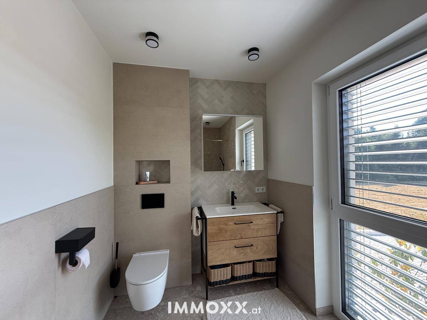 Modernes Badezimmer mit WC, Einzelwaschbecken und Fenster mit Jalousien, in hellen Tönen gehalten.