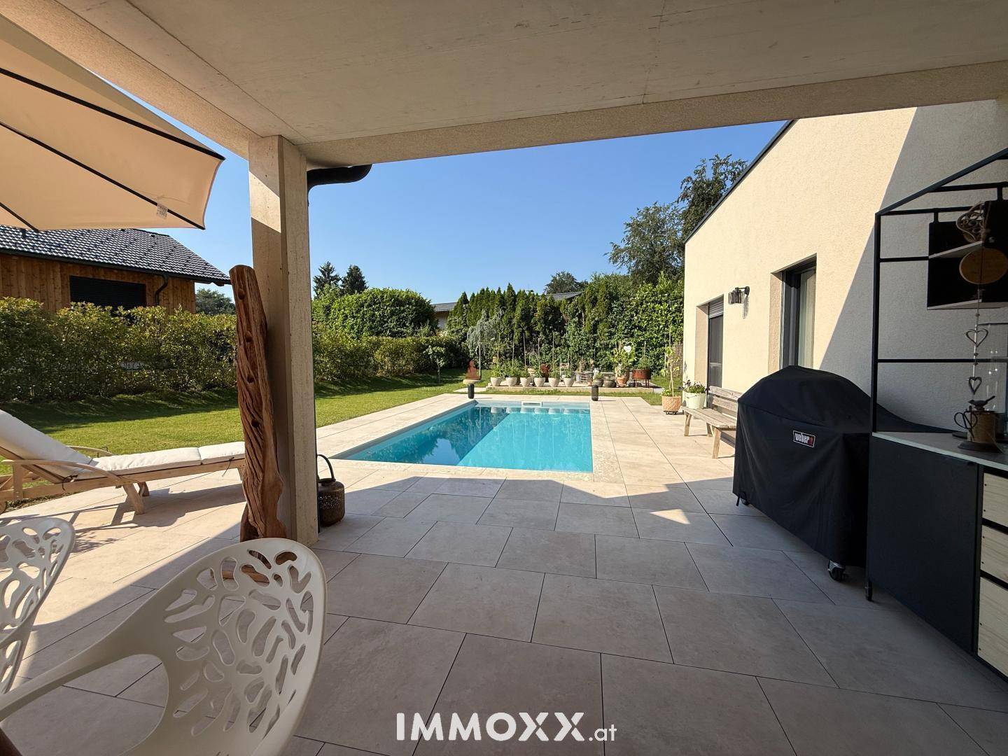 Überdachte Terrasse mit Sitzgelegenheiten, Grillbereich und Blick auf den Pool und den Garten.