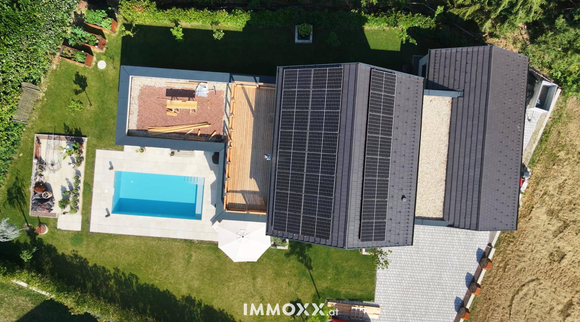 Dachansicht des Hauses mit Photovoltaikanlage, Holzterrasse und Swimmingpool im Gartenbereich.