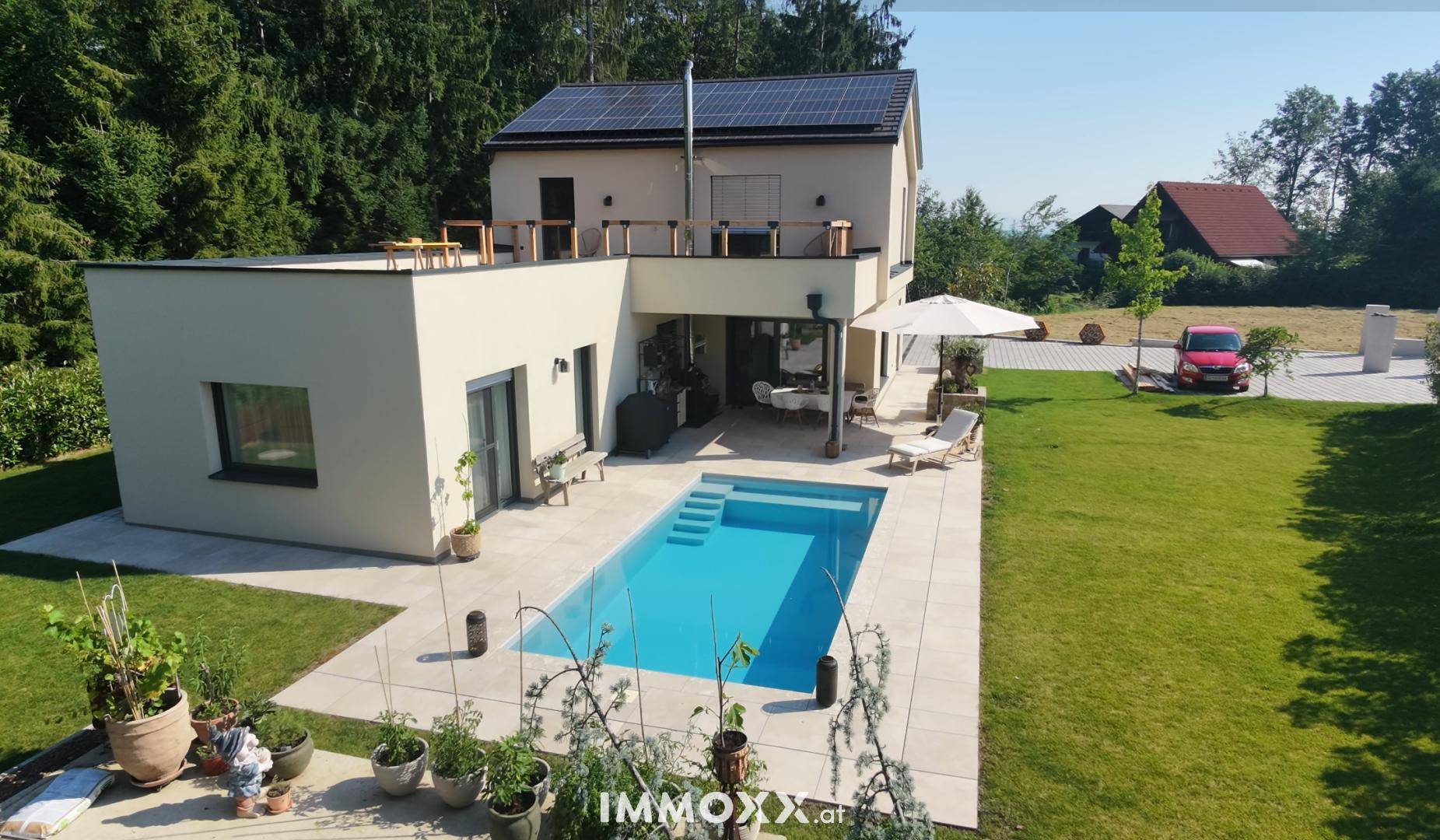 Modernes Haus mit Swimmingpool, überdachtem Sitzbereich und Dachterrasse, umgeben von Grün.