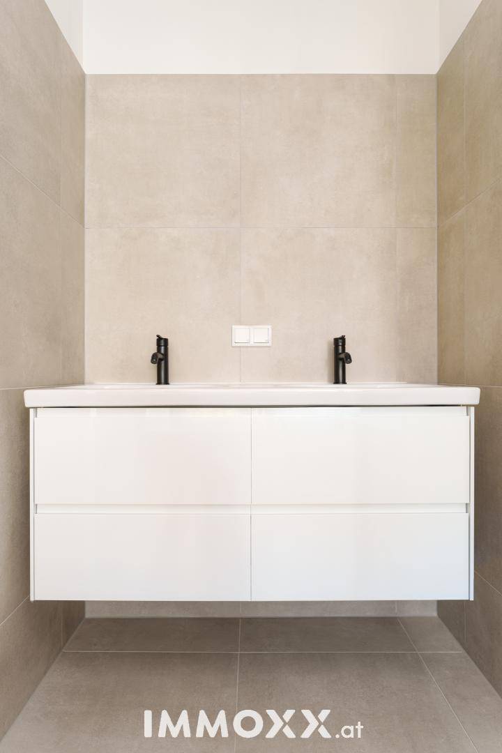 Modernes Badezimmer mit Doppelwaschbecken, schwebendem Unterschrank und hellen Wandfliesen.
