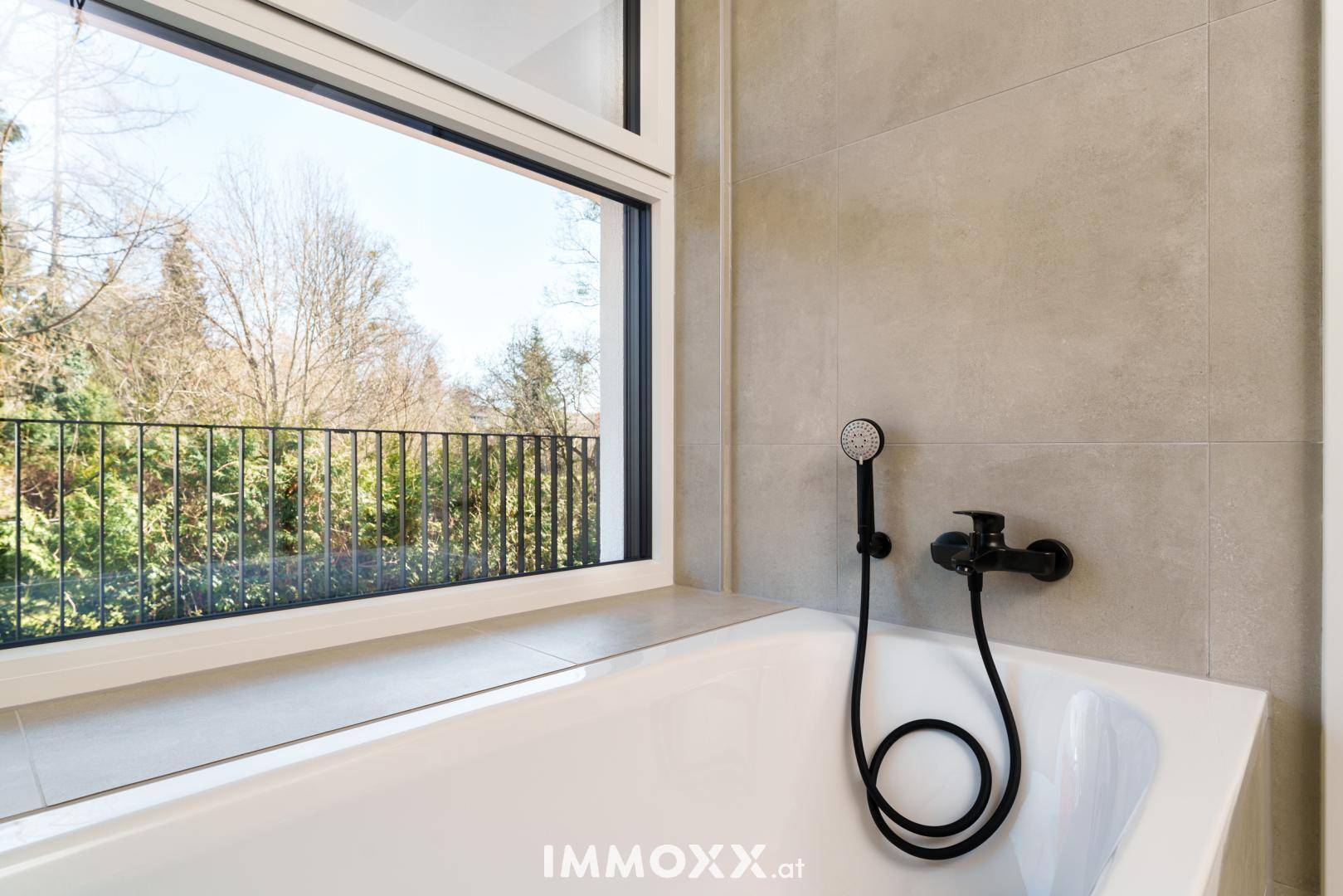 Helles Badezimmer mit Badewanne, modernen Armaturen und Blick ins Grüne durch das Fenster.