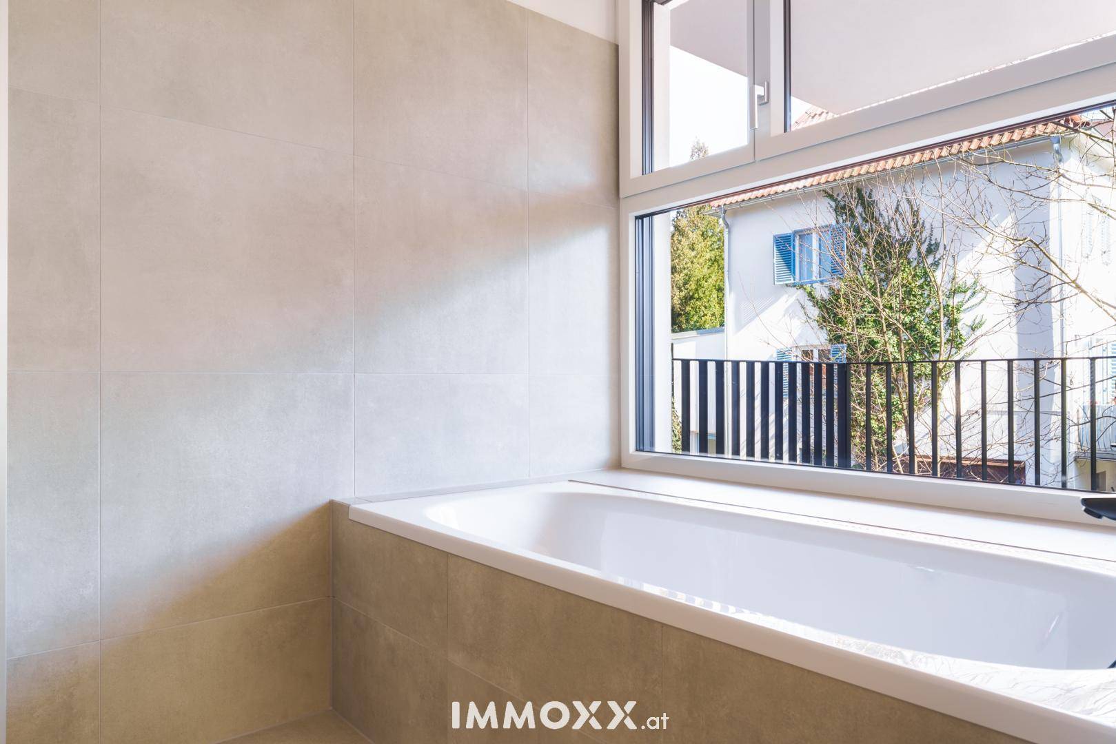 Modernes Badezimmer mit eingebauter Badewanne, hellen Fliesen und großem Fenster.