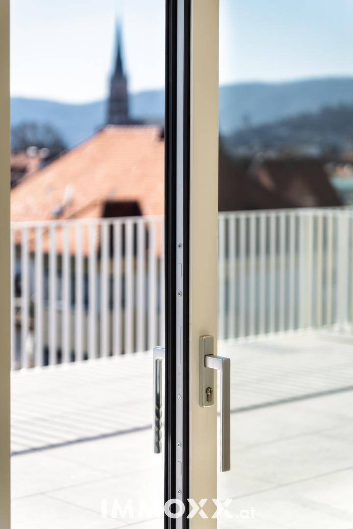 Detailaufnahme einer Balkontür mit Blick auf eine Kirchturmspitze und die Dächer der Stadt.