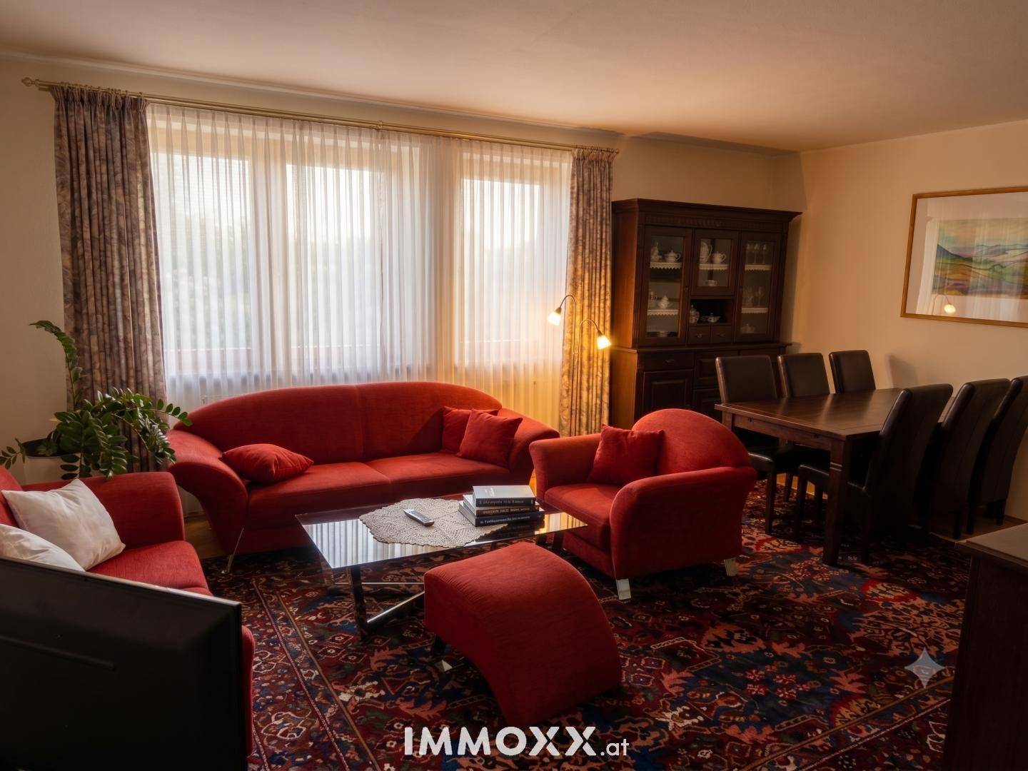 Klassischer Wohn-Essbereich mit roten Sofas, einem Esstisch und großen Fenstern für viel Licht.