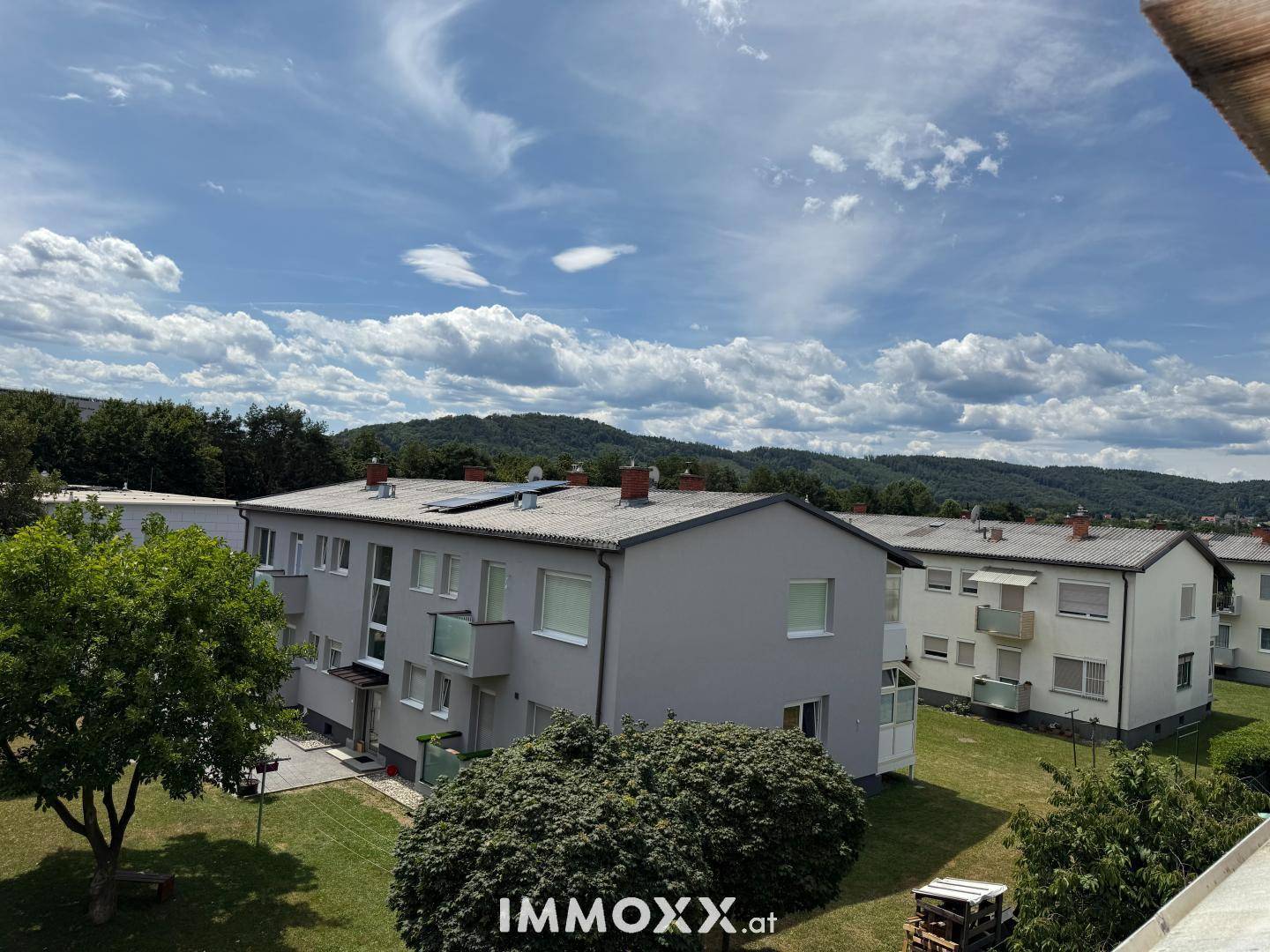 Mehrere Wohngebäude mit grünen Rasenflächen und Bäumen unter einem weiten Himmel mit Wolken.