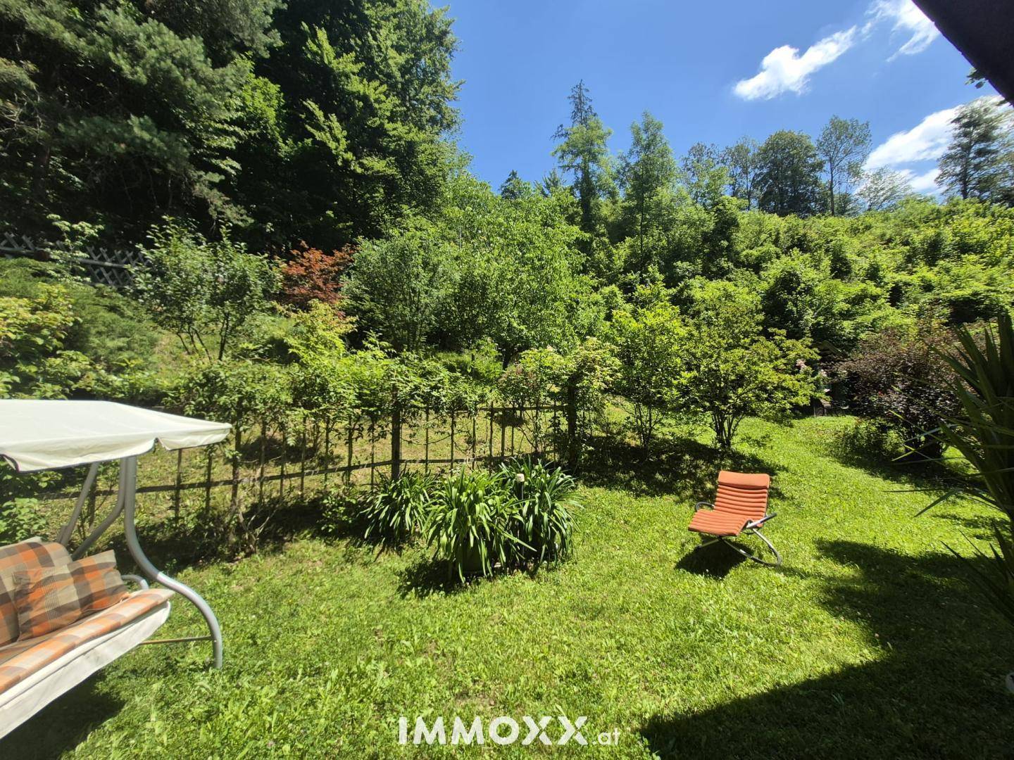 Gepflegter Garten mit Rasenfläche, Bäumen und einer Schaukel, umgeben von viel Grün.