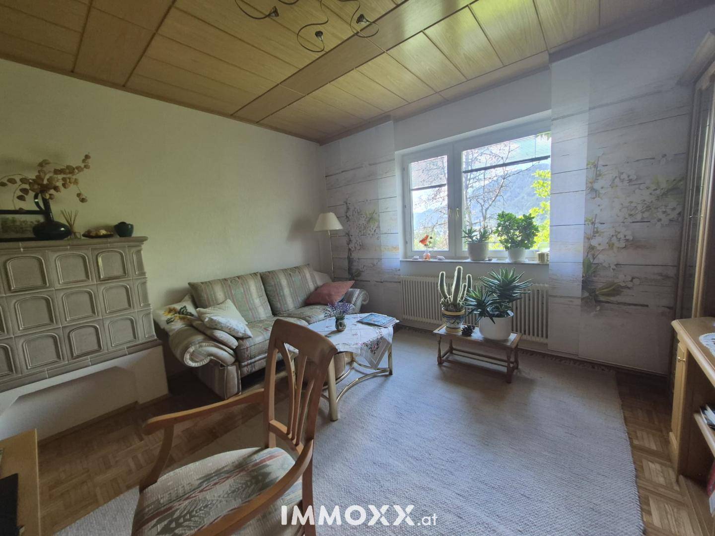 Gemütliches Schlafzimmer mit Parkettboden, Sofa und großem Fenster mit Blick ins Grüne.