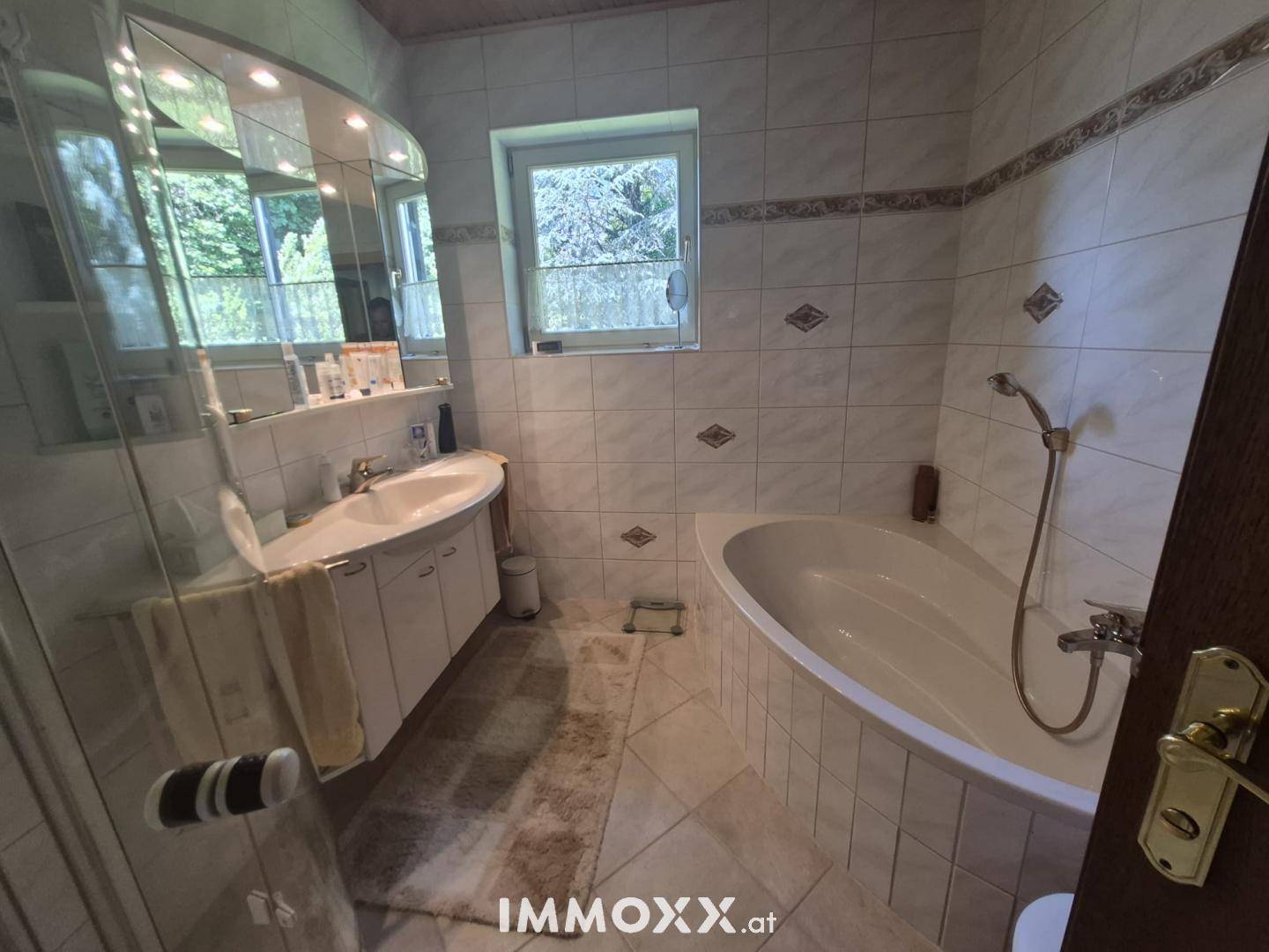 Helles Badezimmer mit weißen Fliesen, Badewanne und Doppelwaschbecken unter einem großen Spiegel.