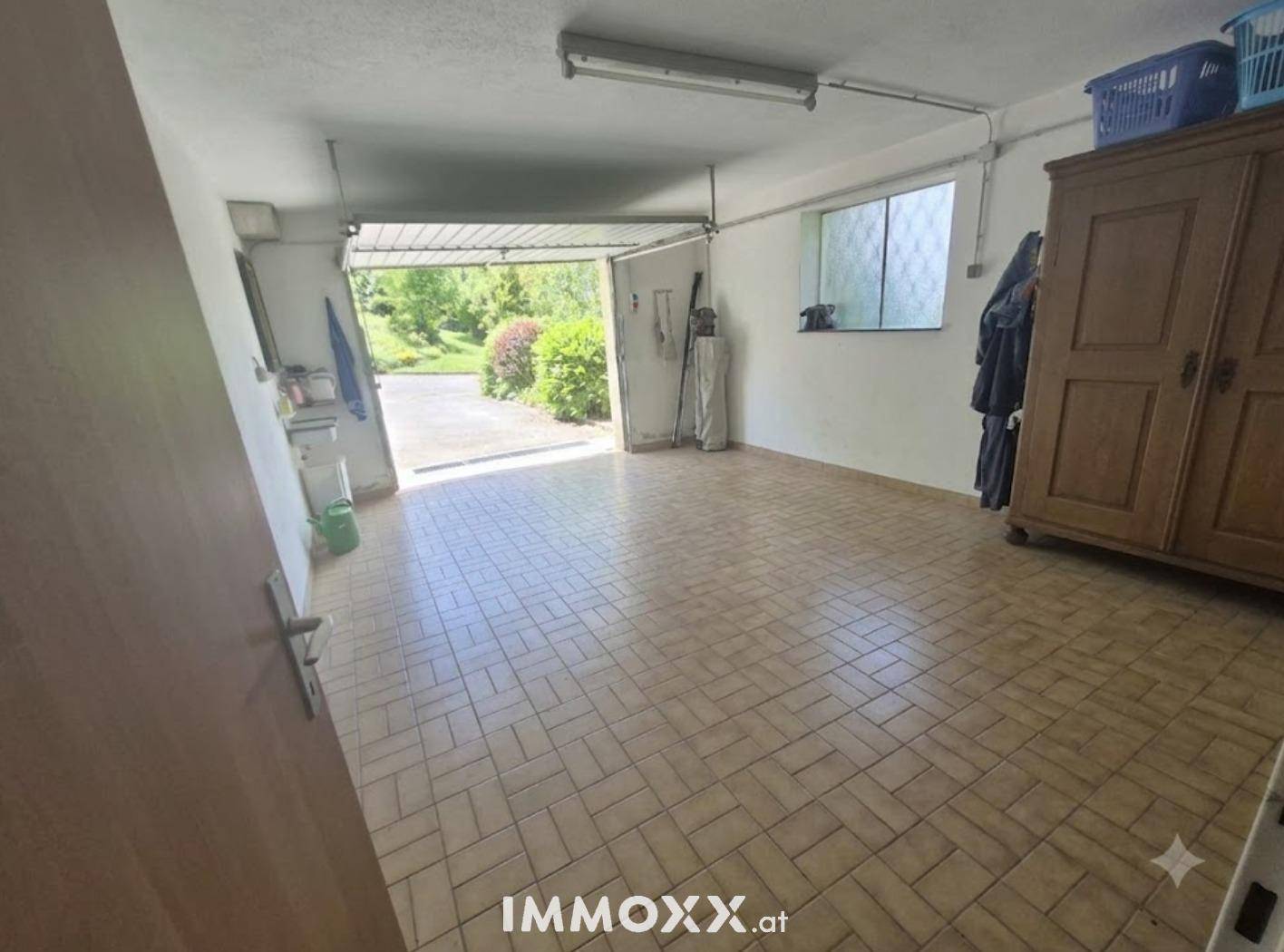 Geräumige Garage mit Fliesenboden und offenem Tor zum Außenbereich, genutzt als Abstellraum.