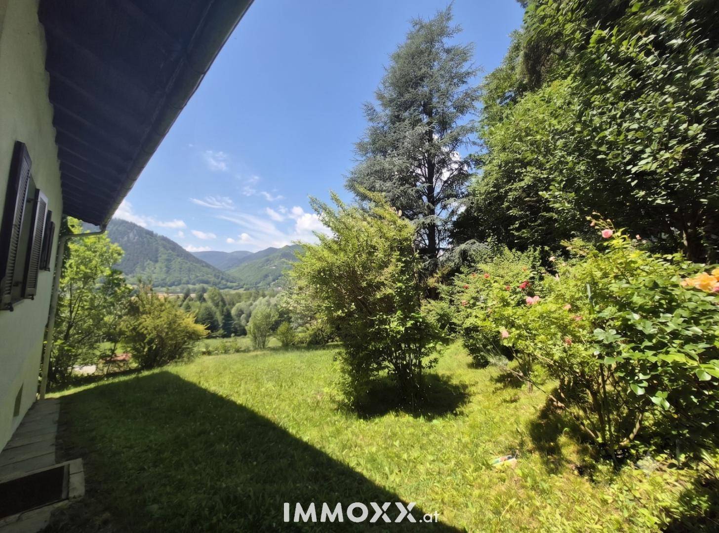 Seitlicher Blick auf das Haus und den weitläufigen Garten mit Rasen und Sträuchern.