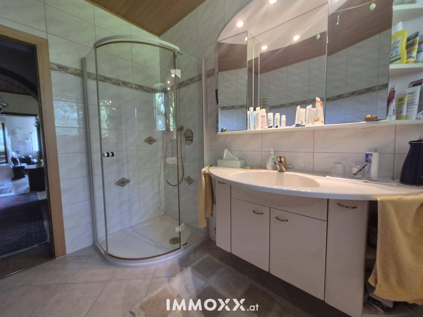 Badezimmer mit Eckdusche, Einzelwaschbecken und großem Spiegelschrank, hell gefliest.