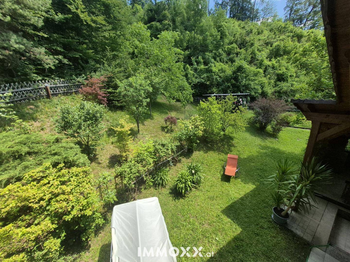 Blick von oben auf den weitläufigen Garten mit Rasen, Bäumen und einer Sonnenliege.