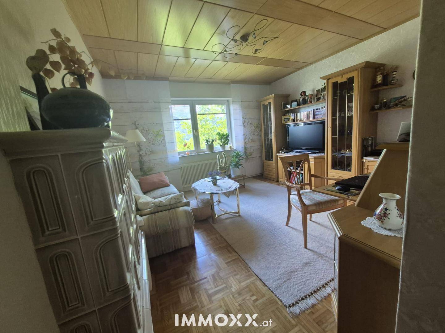 Helles Schlafzimmer mit Parkettboden, Holzdecke und einem traditionellen Kachelofen.