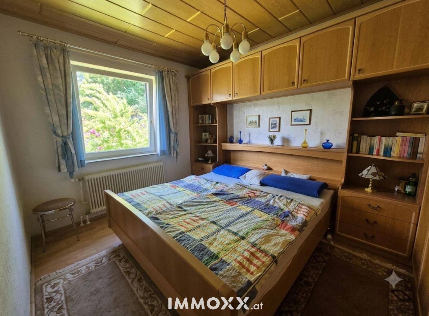 Gemütliches Schlafzimmer mit Holzdecke, Einbauschränken und Blick ins Grüne durch das Fenster.