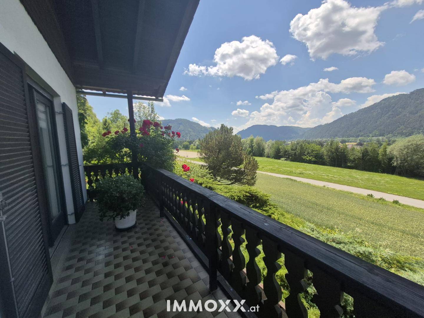 Gemütlicher Balkon mit Holzbalkongeländer und weitem Blick über das Tal und die Berge.