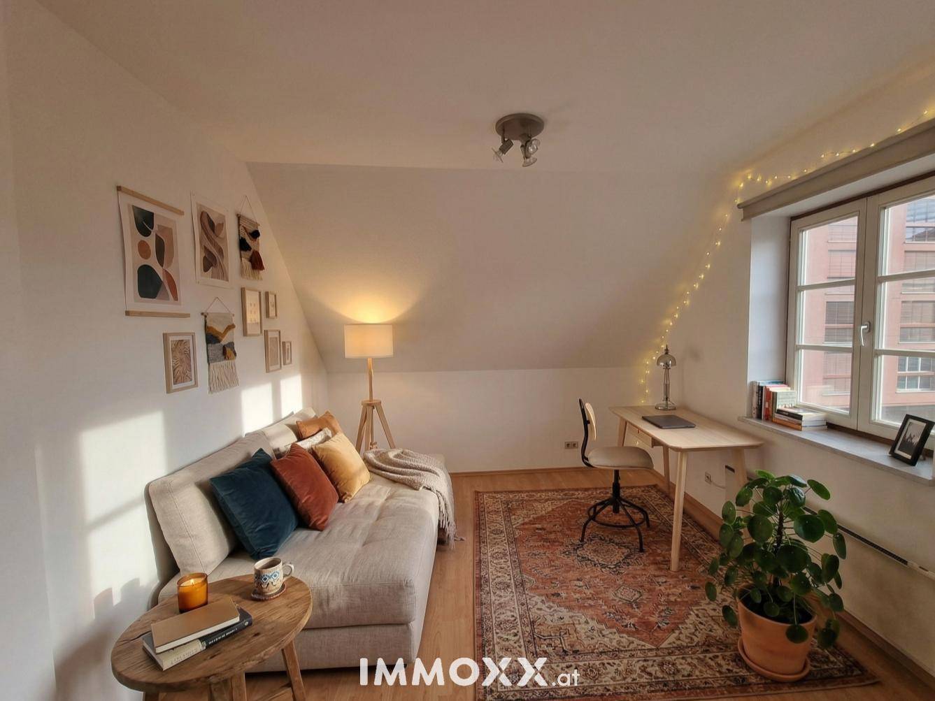 Gemütliches Schlafzimmer mit Dachschräge, Schreibtisch und dekorativer Beleuchtung, ideal als Gästezimmer oder Büro.