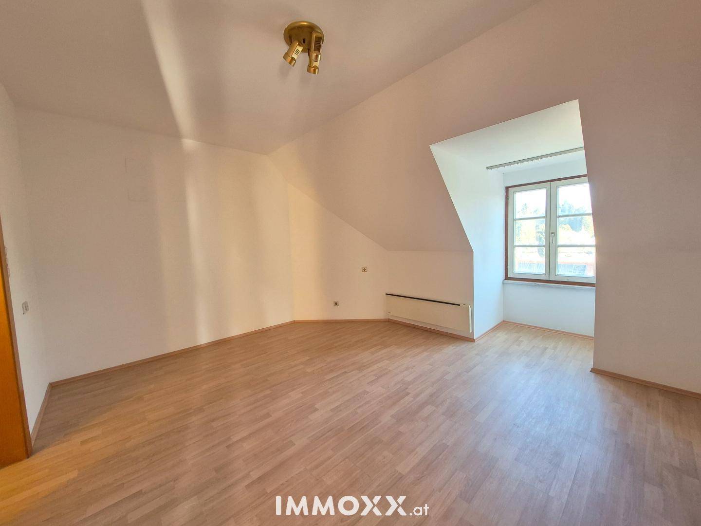 Leeres Zimmer mit Dachschräge und Laminatboden, bereit für individuelle Einrichtung und Nutzung.