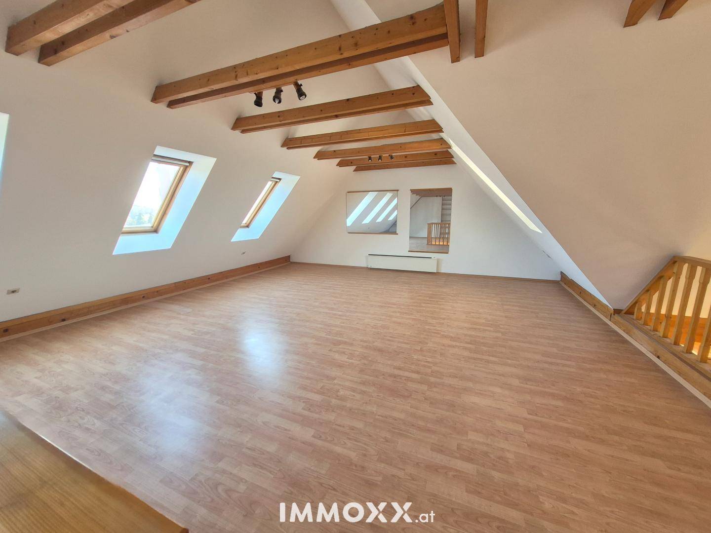 Großzügiger offener Raum mit Holzbalken, Dachfenstern und Laminatboden, ideal für Wohnzwecke.