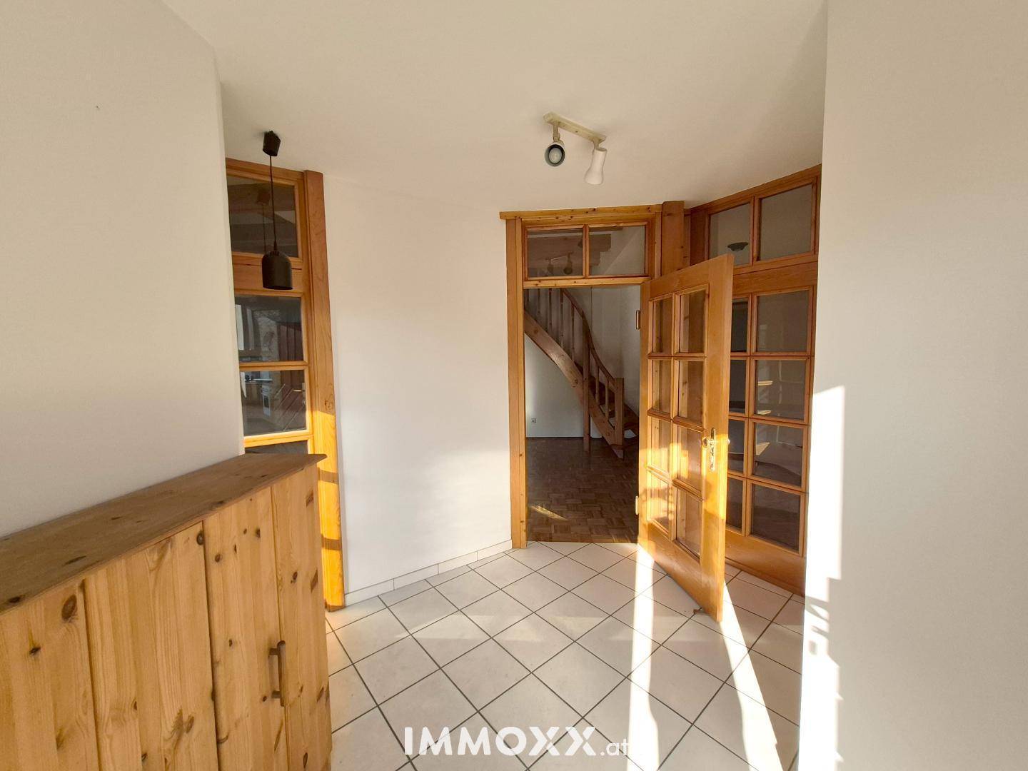 Heller Flur mit Fliesenboden und Holztüren, der zu weiteren Räumen und einer Treppe führt.