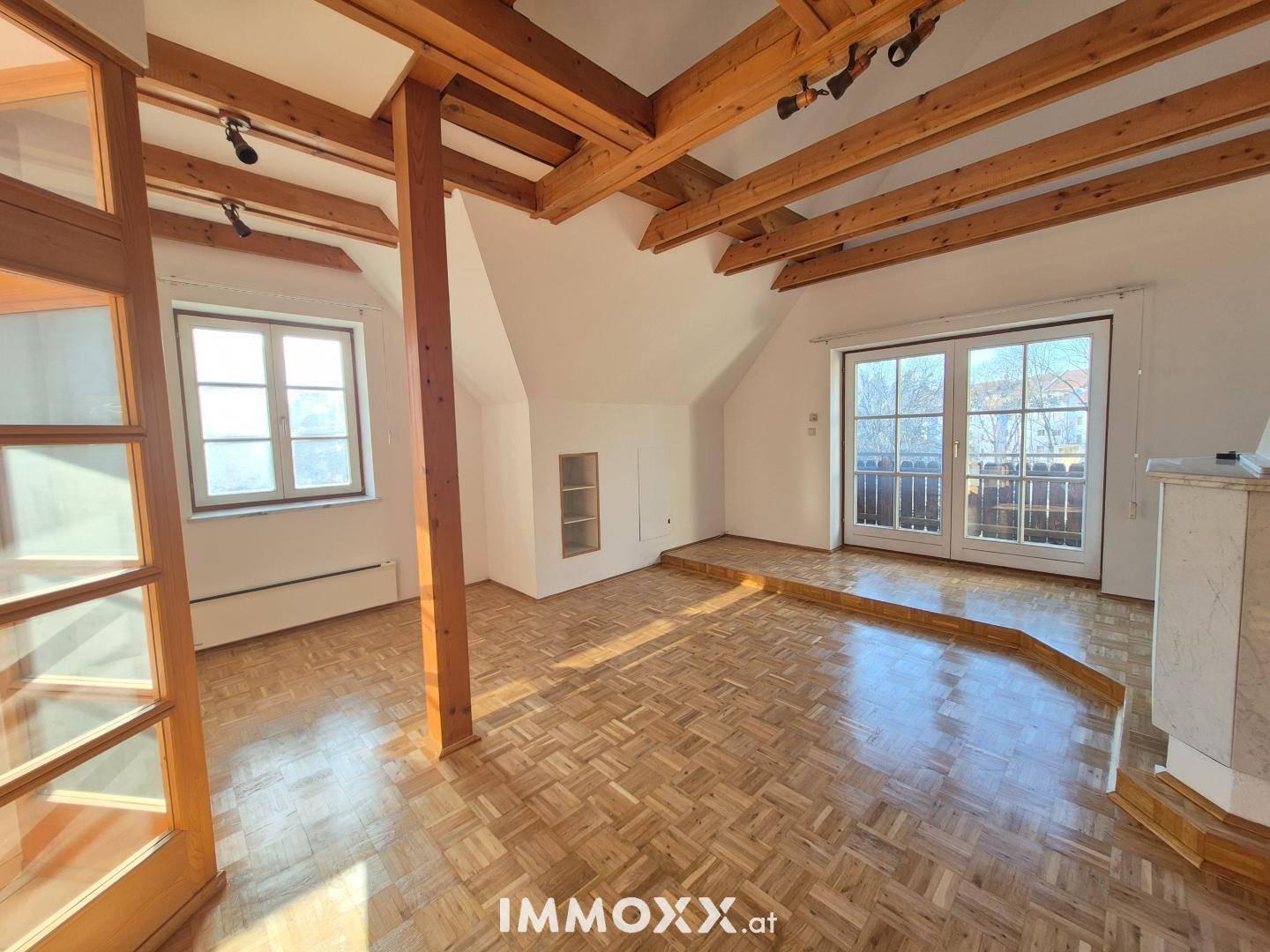 Heller Wohnbereich mit Holzbalken, Kamin und Zugang zu einem Balkon, der viel Licht bietet.