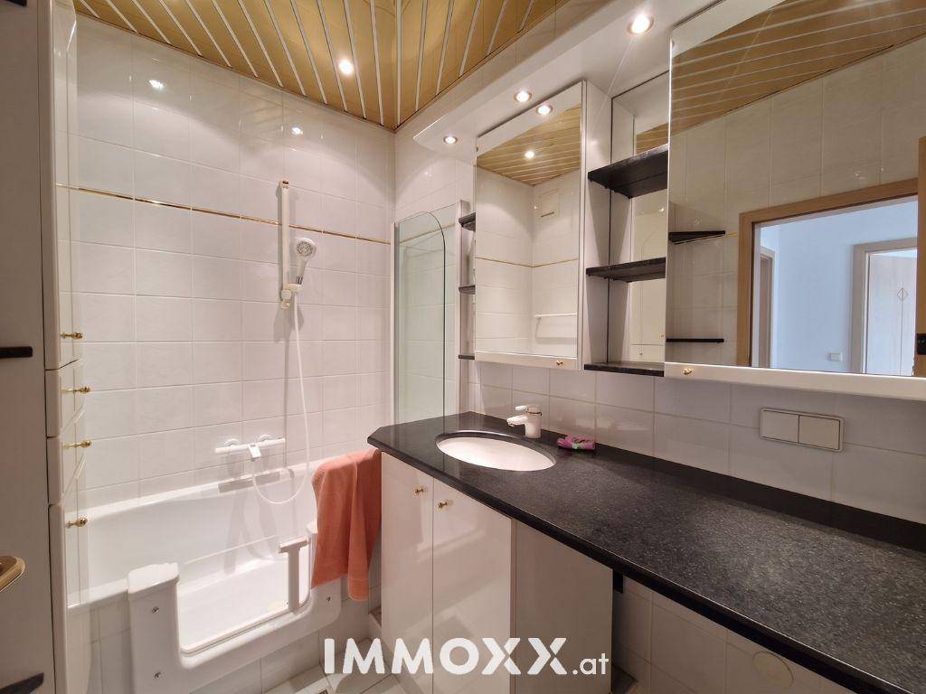 Badezimmer mit Badewanne, Einzelwaschbecken auf Granitplatte und Spiegelschrank.