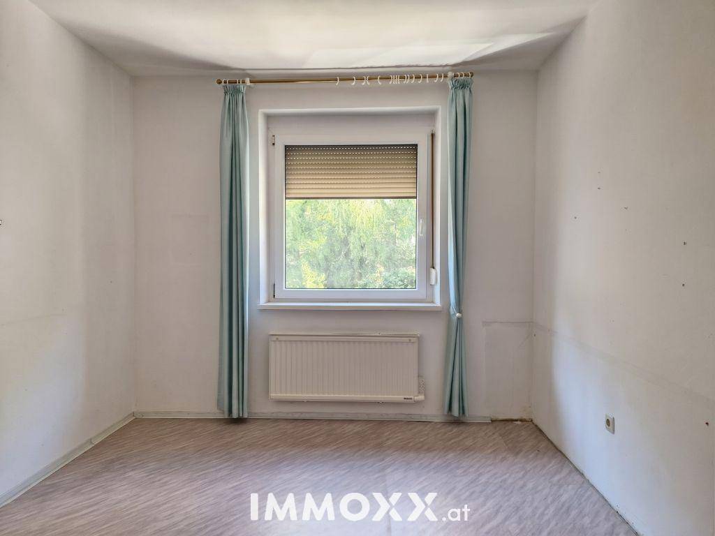 Leeres Zimmer mit hellem Laminatboden, Fenster und Heizkörper.