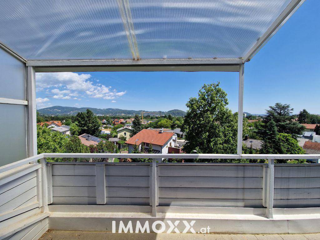 Überdachter Balkon mit weitem Blick über die grüne Umgebung und die Dächer der Häuser.