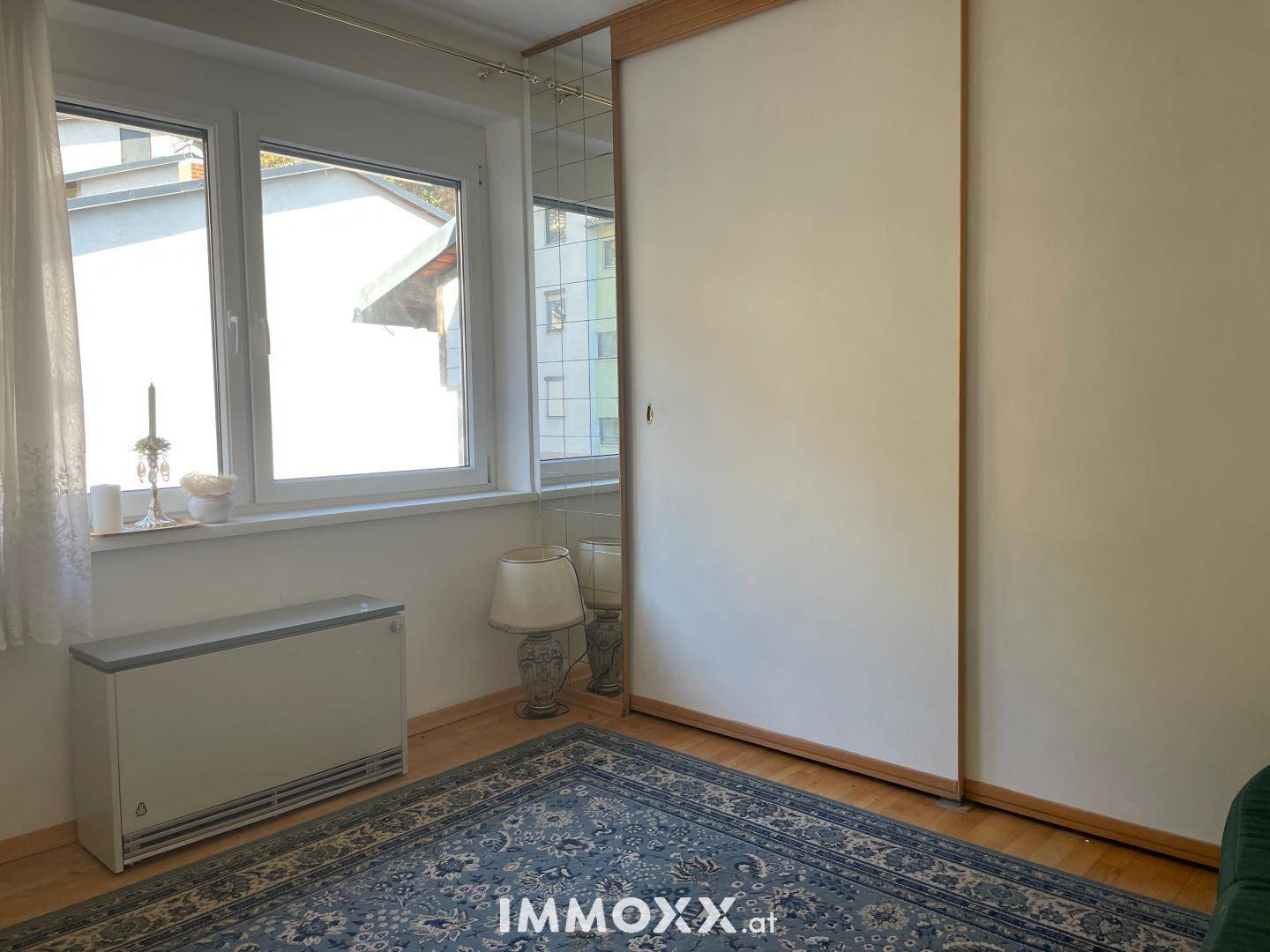 Helles Zimmer mit großem Fenster, Teppichboden und einem geräumigen Spiegelschrank.