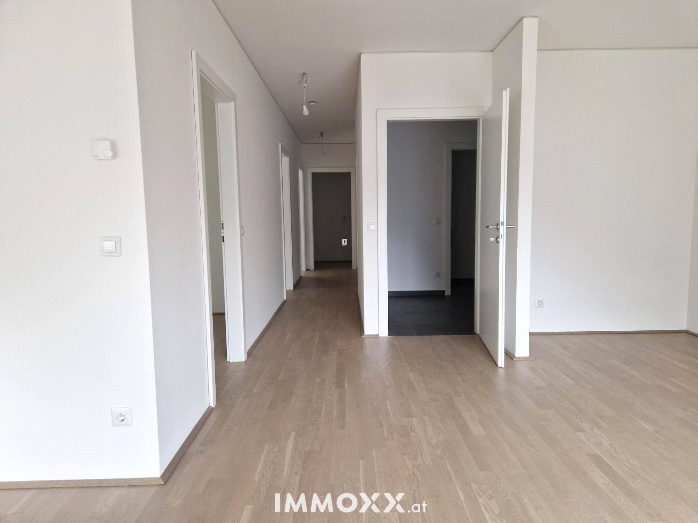 Heller Flur mit Holzboden und mehreren Türen zu angrenzenden Räumen in einem modernen Gebäude.
