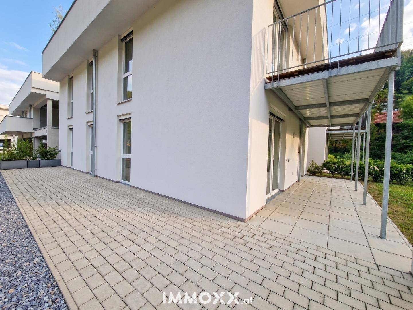 Moderne Gebäudefassade mit großen Fenstern und Balkonen, eingebettet in eine grüne Umgebung.