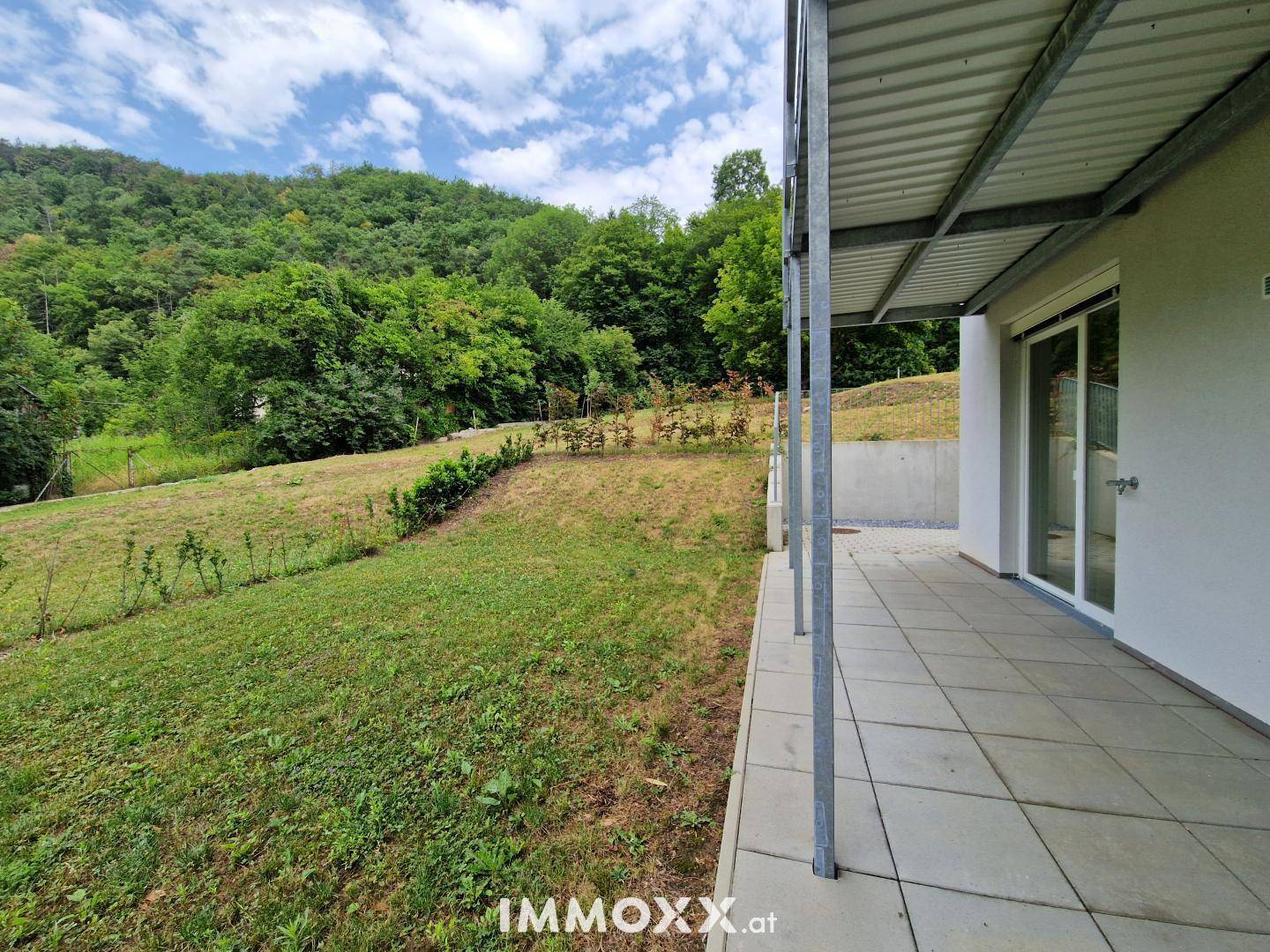 Weitläufiger Gartenbereich mit Rasenfläche und gepflasterter Terrasse, umgeben von Bäumen und Natur.