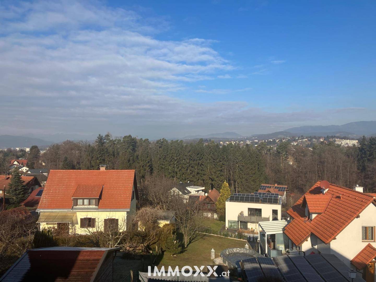 Blick über eine Wohngegend mit Einfamilienhäusern, Gärten und bewaldeten Hügeln in der Ferne.