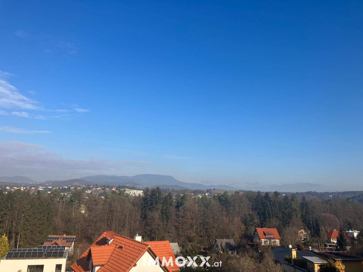Panoramablick über eine grüne Landschaft mit Häusern und einer Bergkette am Horizont.