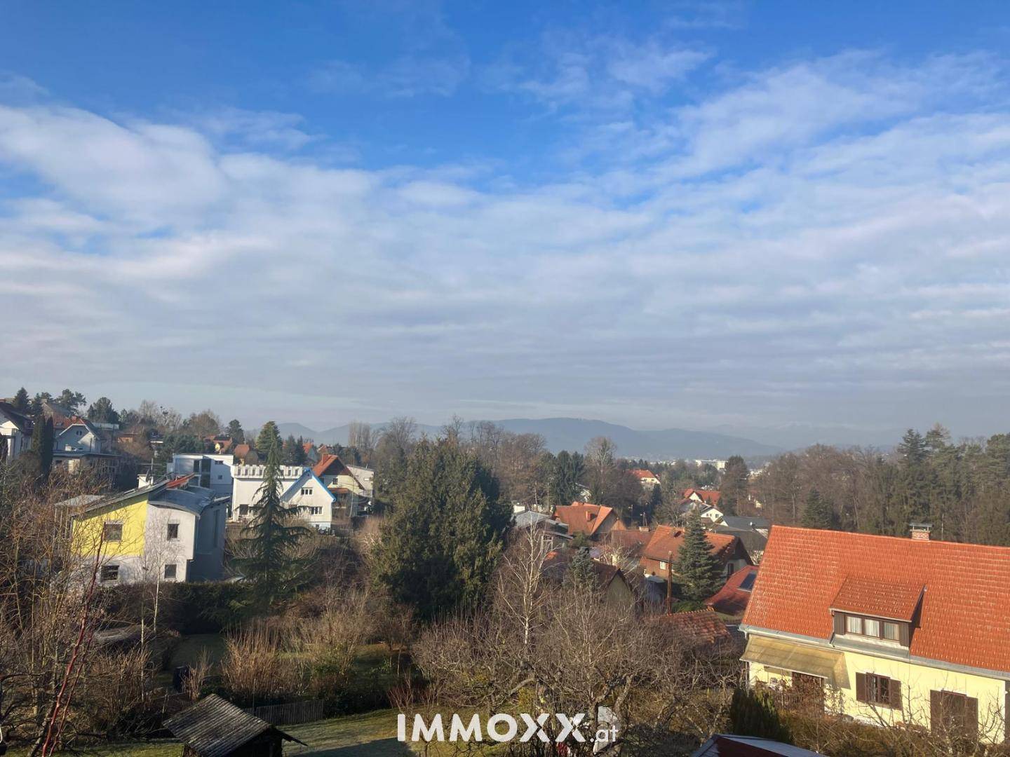 Weitläufiger Blick über eine Wohnsiedlung mit vielen Bäumen und Bergen im Hintergrund.