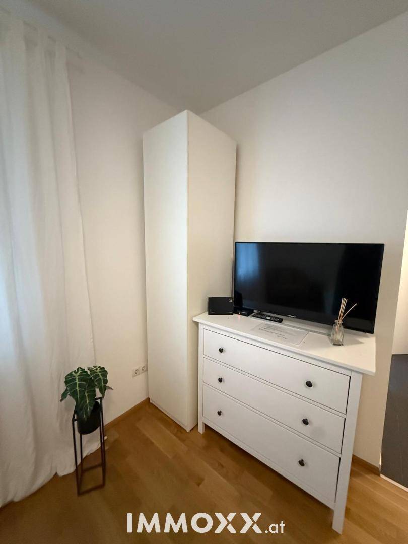 Ecke eines Zimmers mit weißer Kommode und Flachbildfernseher, schlicht eingerichtet.