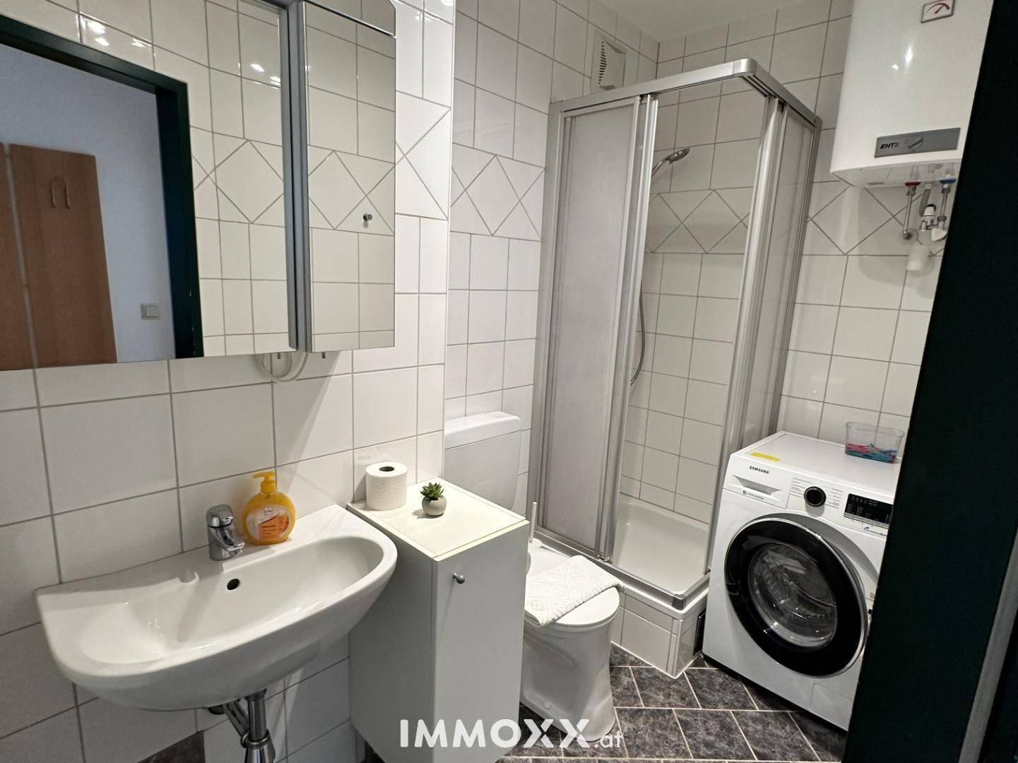 Modernes Badezimmer mit Duschkabine, Waschbecken, Toilette und Waschmaschine, hell gefliest.