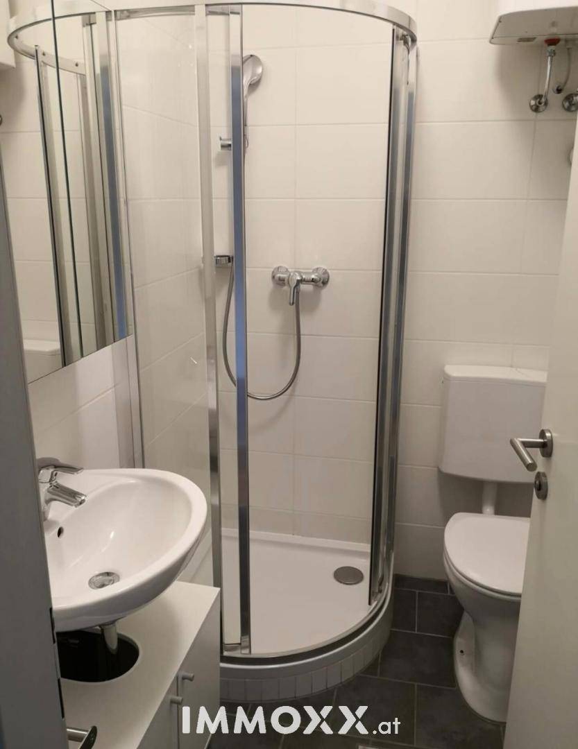 Funktionales Badezimmer mit Duschkabine, Waschbecken und Toilette in hellen Fliesen.