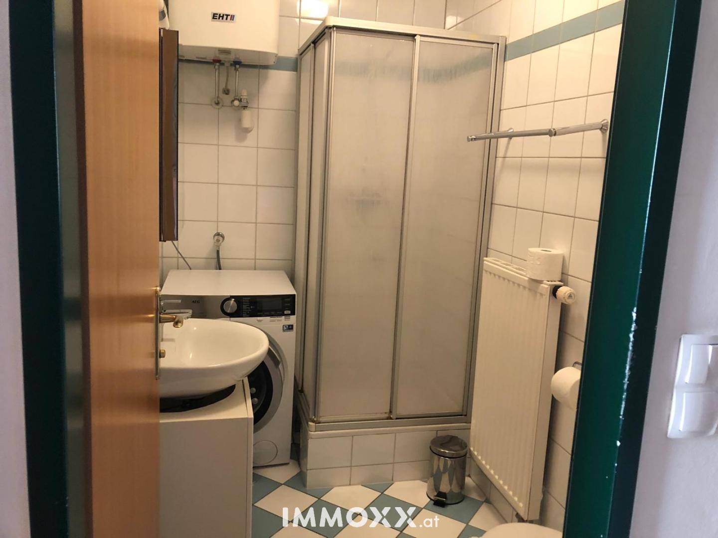 Badezimmer mit Duschkabine, Waschbecken, Toilette und Waschmaschine auf kariertem Boden.