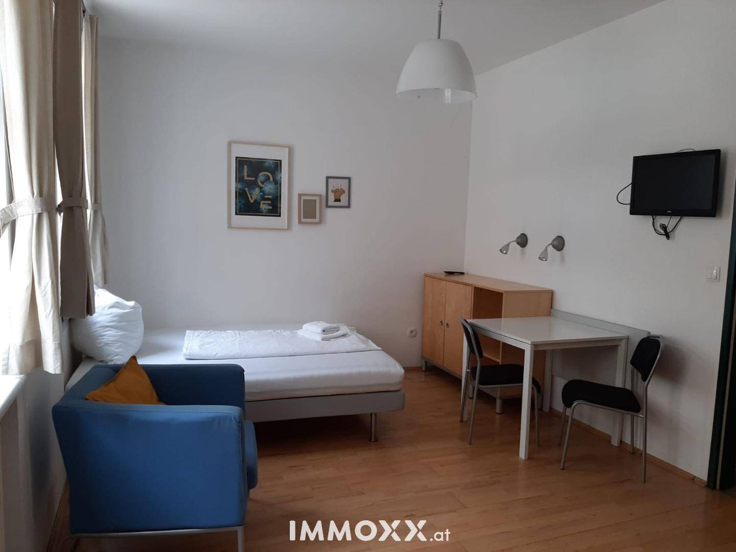 Kombinierter Wohn- und Schlafbereich mit Esstisch, Bett und kleiner Sitzecke, hell und modern.