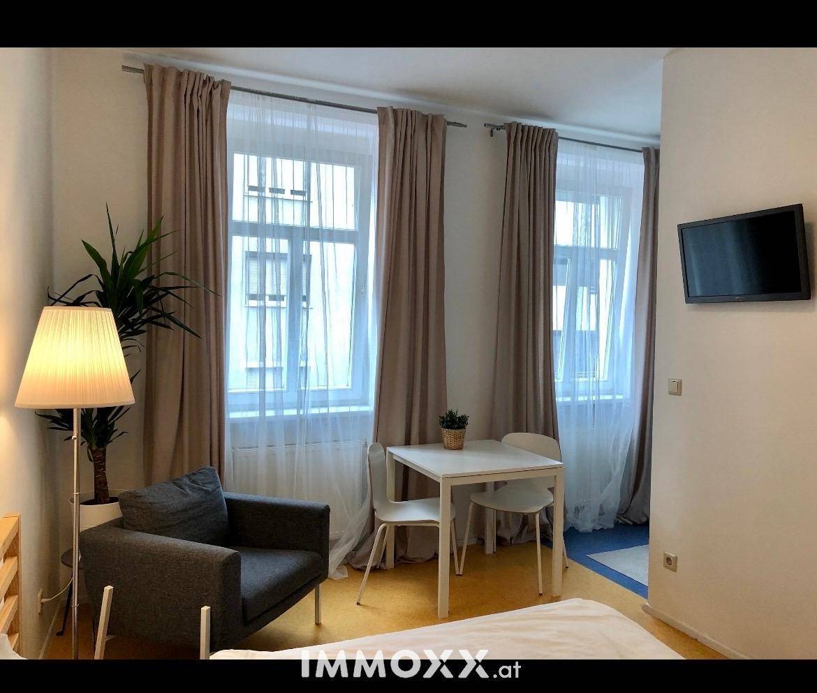 Heller Wohn- und Schlafbereich mit Bett, Sessel, Esstisch und zwei großen Fenstern.
