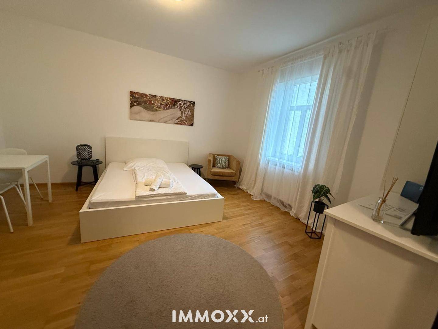 Helles Schlafzimmer mit Holzboden, großem Fenster und moderner Einrichtung.