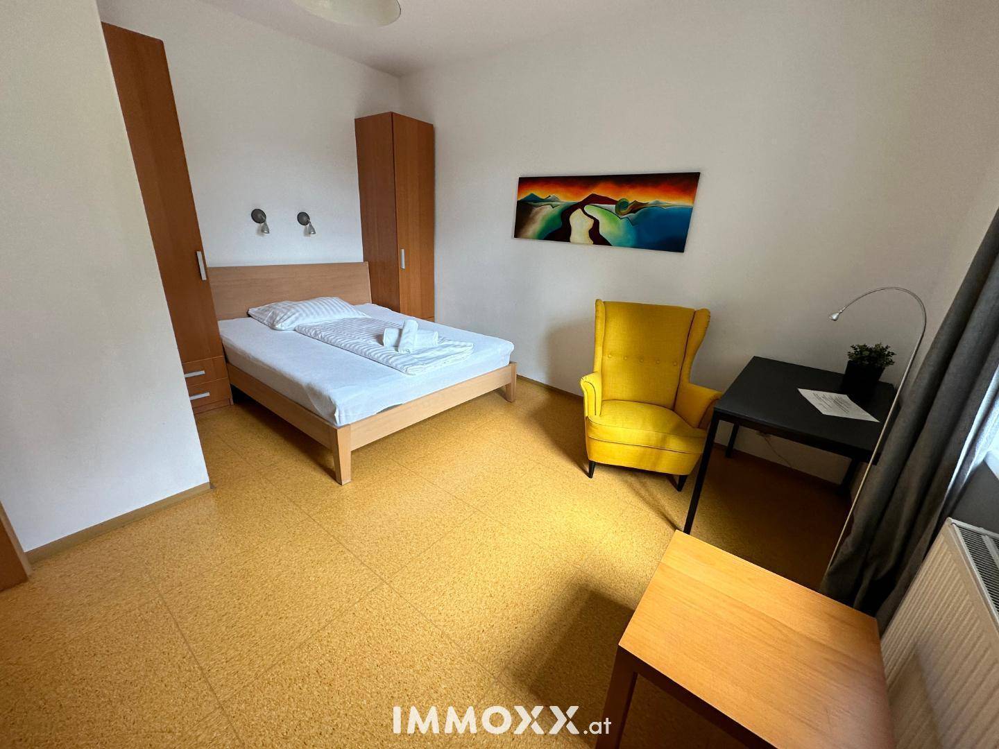 Helles Schlafzimmer mit Holzbett, gelbem Sessel und Kleiderschrank in freundlicher Atmosphäre.