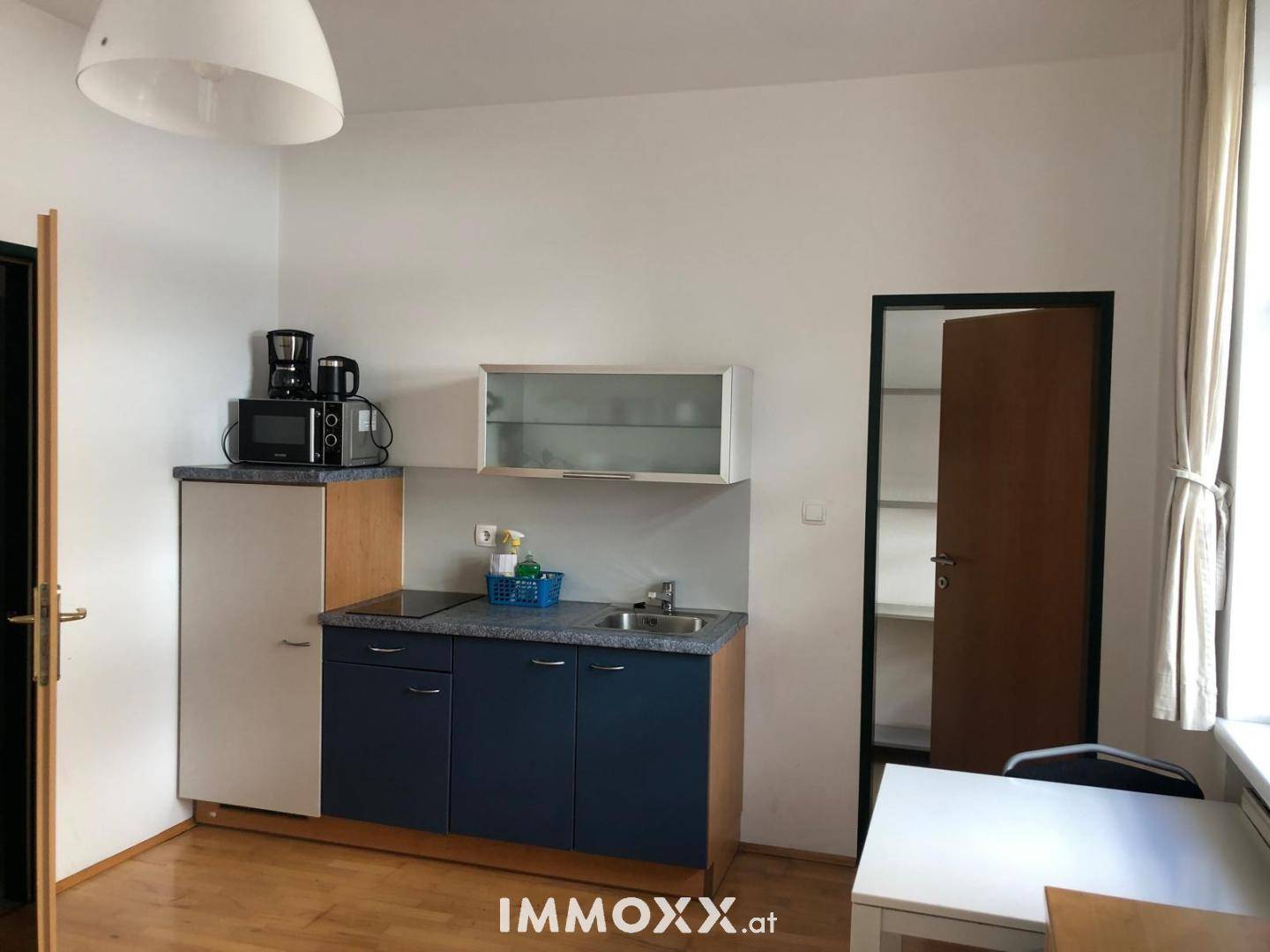 Kleine Kochnische mit blauen Unterschränken, Kühlschrank und Esstisch, funktional und hell.