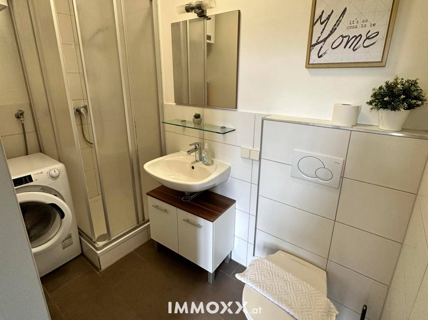 Modernes Badezimmer mit Duschkabine, Waschbecken, Toilette und Waschmaschine, hell gefliest.