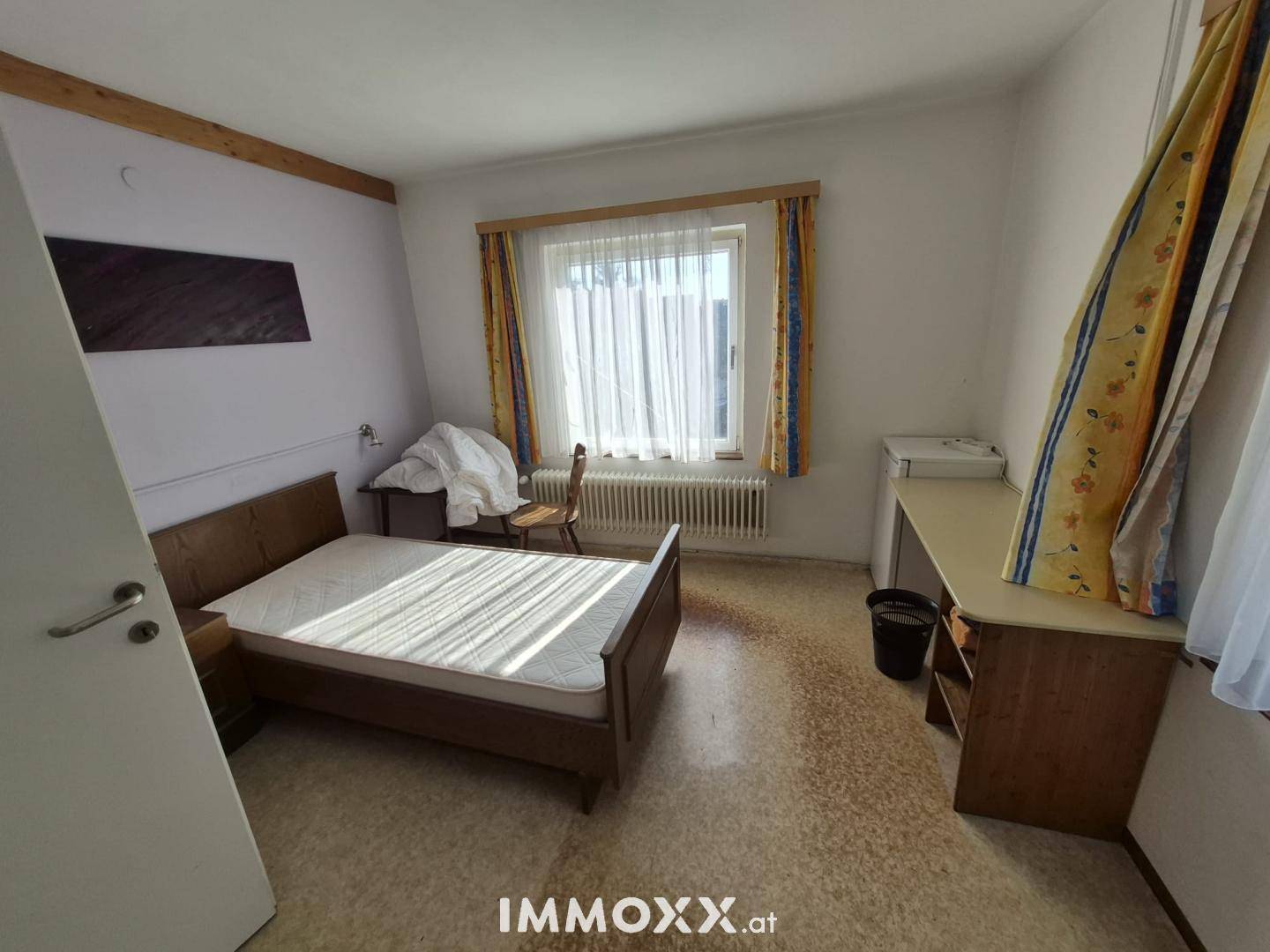 Schlafzimmer mit Doppelbett, Schreibtisch und Fenster mit viel Tageslicht.