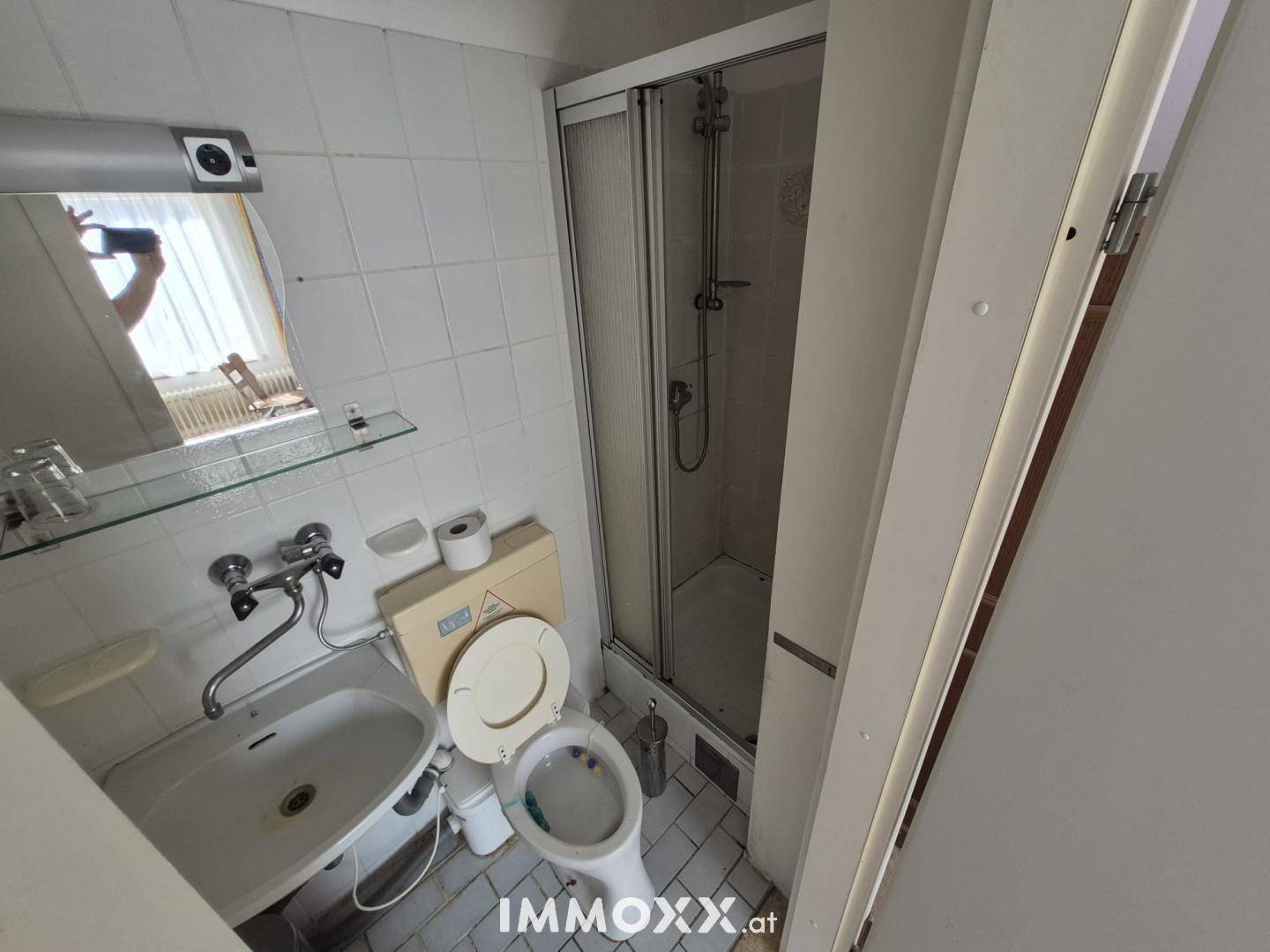 Kleines Badezimmer mit Dusche, WC, Waschbecken und Spiegel.