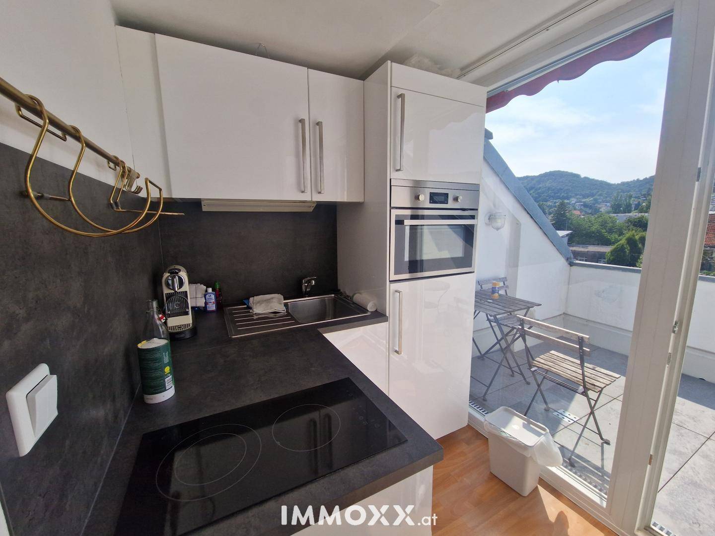 Kompakte Küche mit weißen Hochglanzschränken, Einbauofen und direktem Zugang zur Dachterrasse.