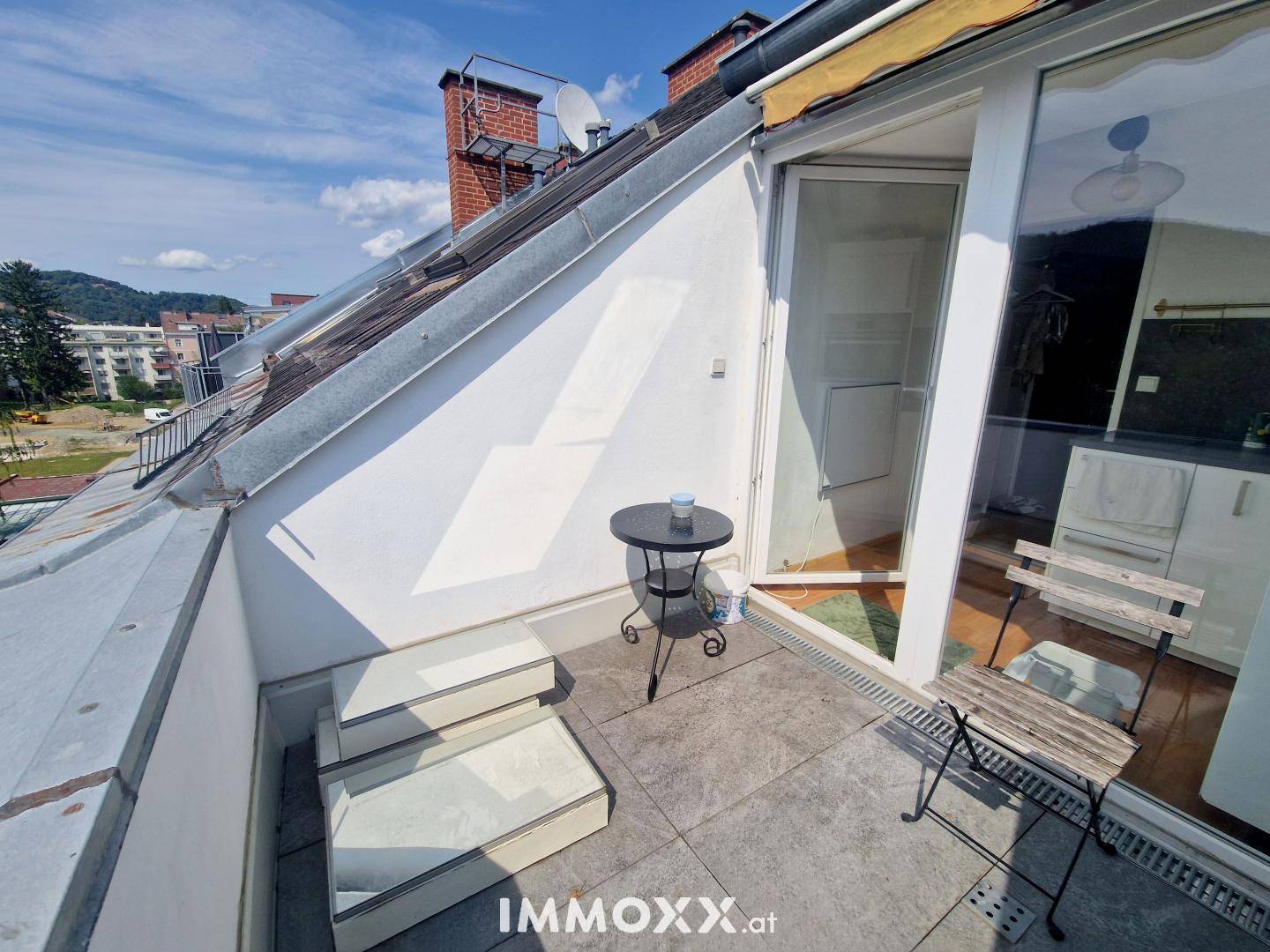 Sonniger Terrassenbereich mit kleinem Tisch und Blick auf die Dächer und die Landschaft.